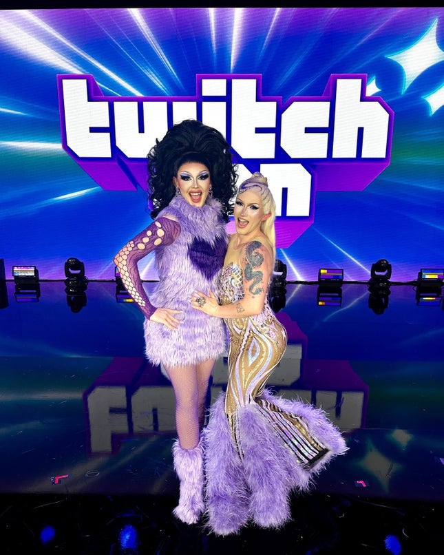 On stage, two beautiful drag queens smile in front of the TwitchCon sign.